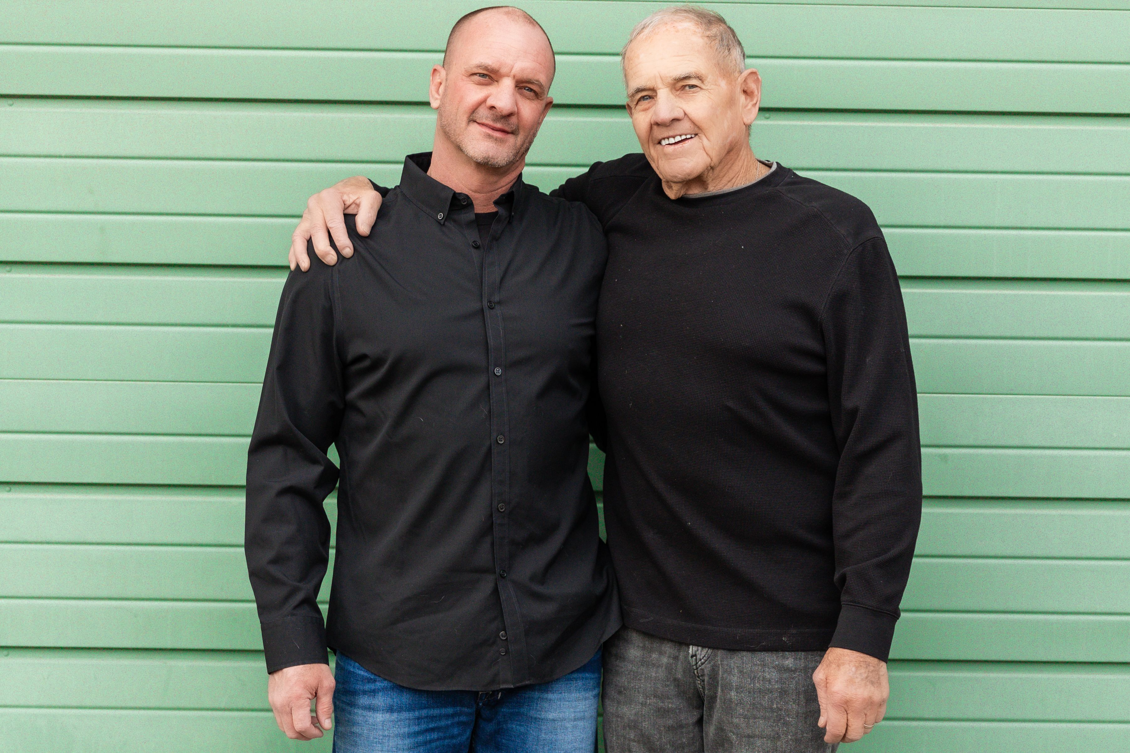 Kip Holmes and his father Steve standing together in front of a green garage door