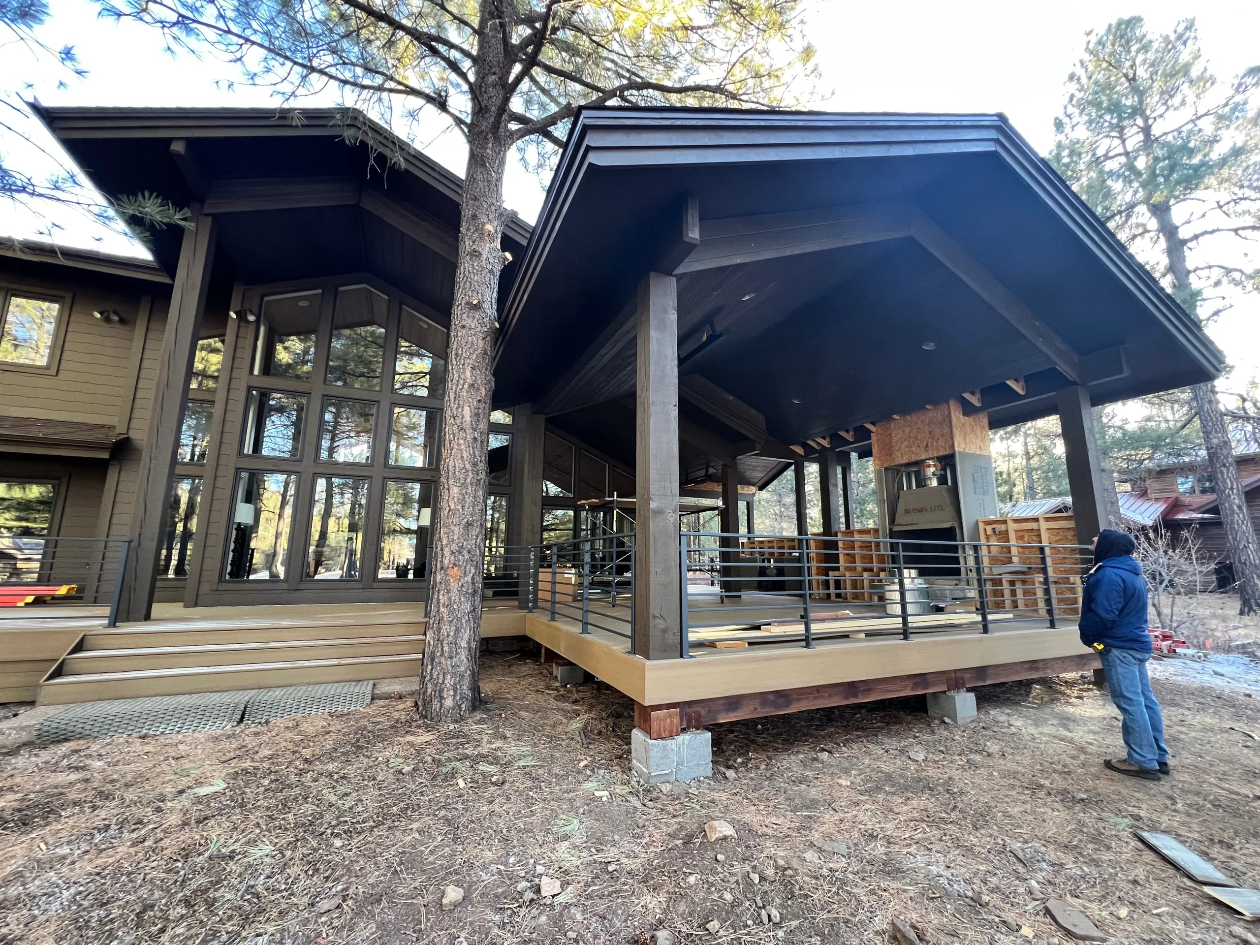New covered deck addition on a dark-sided home among the pines, under construction