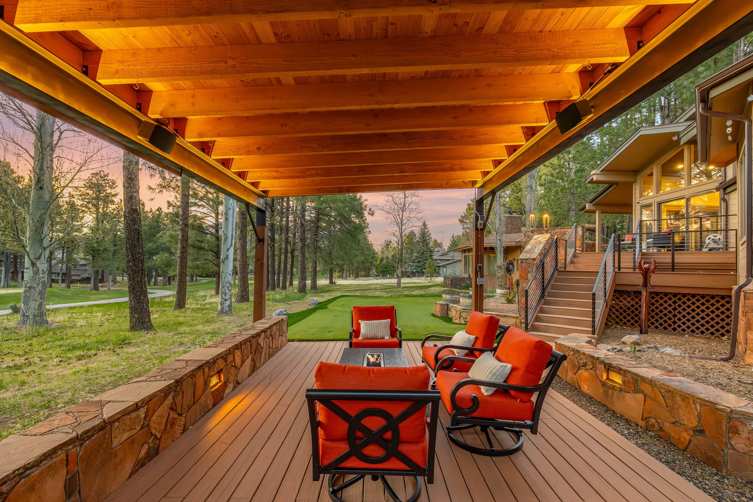 Covered deck with red-cushioned seating and a stone wall at sunset