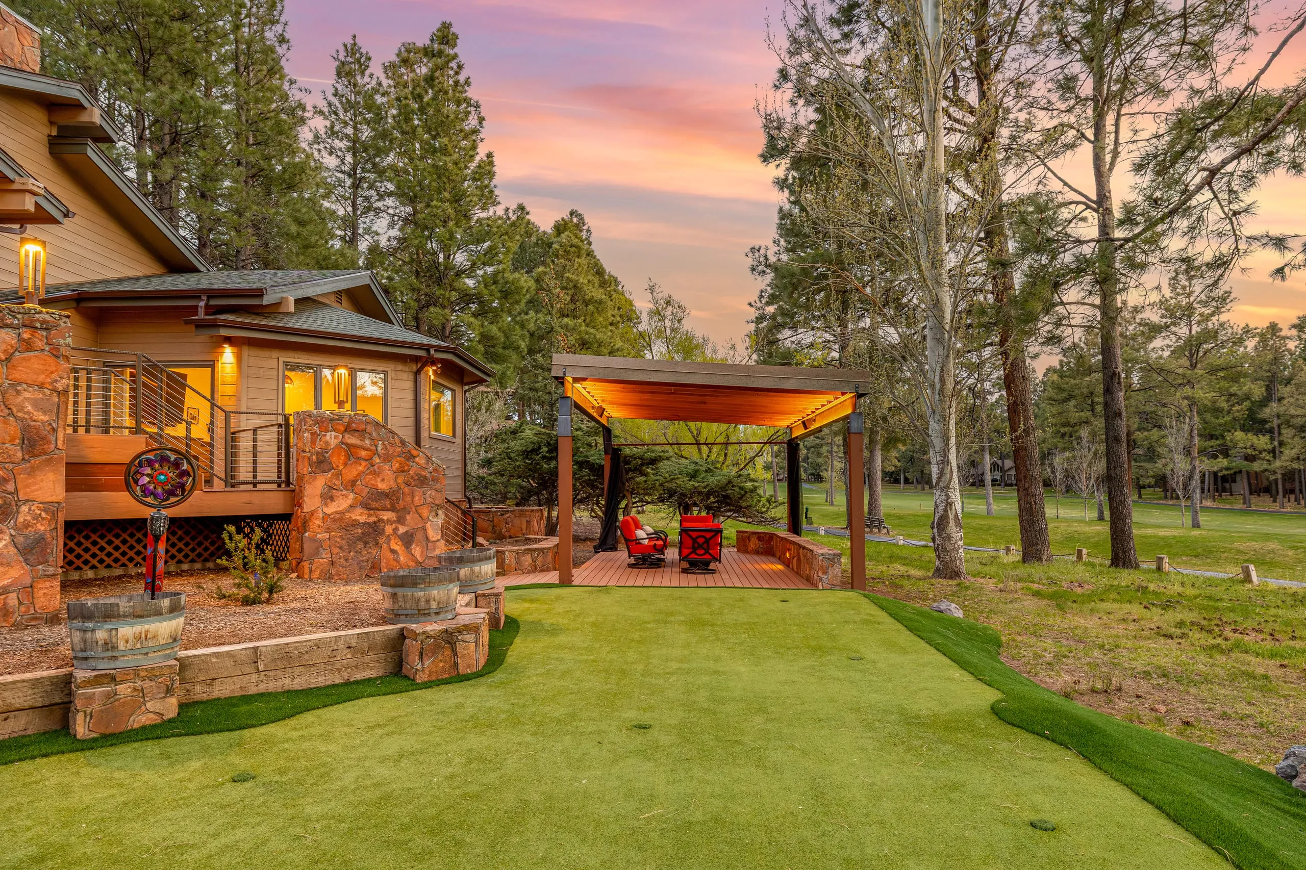 Backyard putting green and covered pavilion beside a stone-faced home at sunset