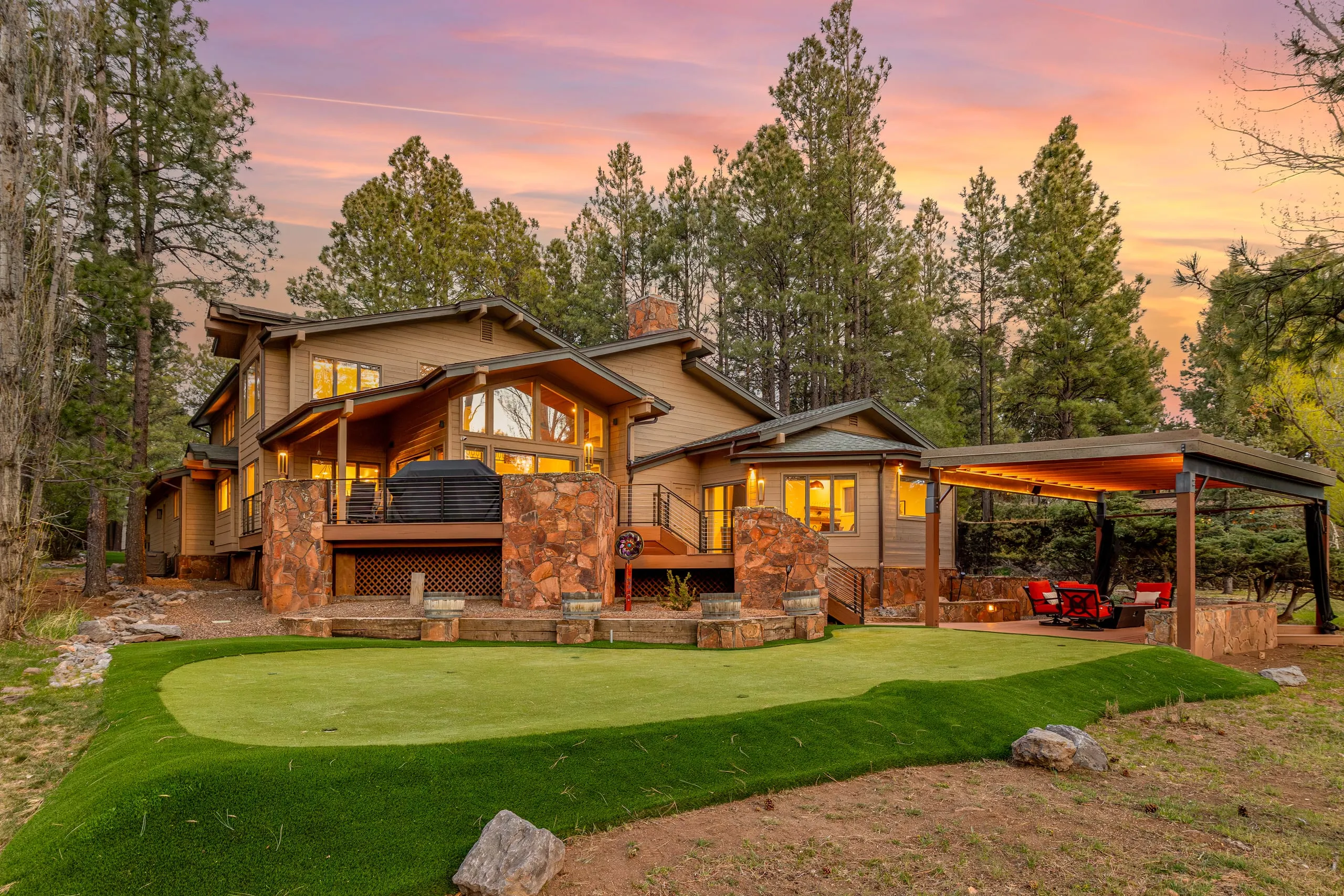 Stone and timber home with a backyard putting green at sunset
