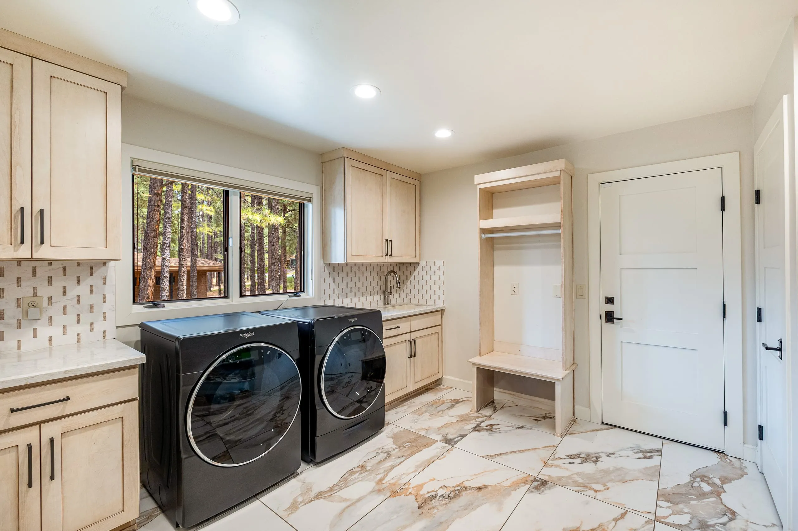 Laundry room with front-loading washer and dryer, light wood cabinets and marble-look tile