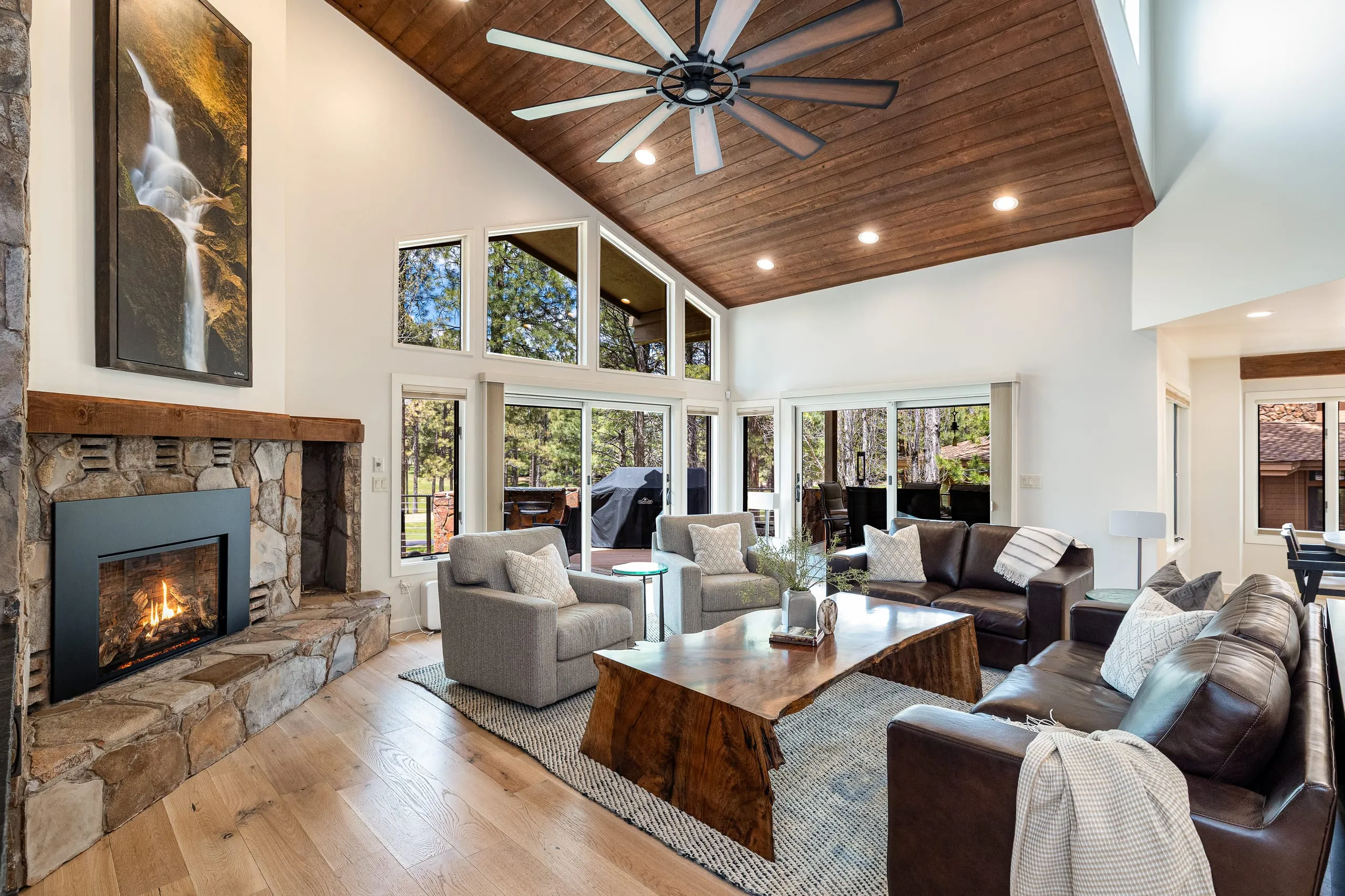 Living room with a stone fireplace, live-edge coffee table and a wood-paneled vaulted ceiling