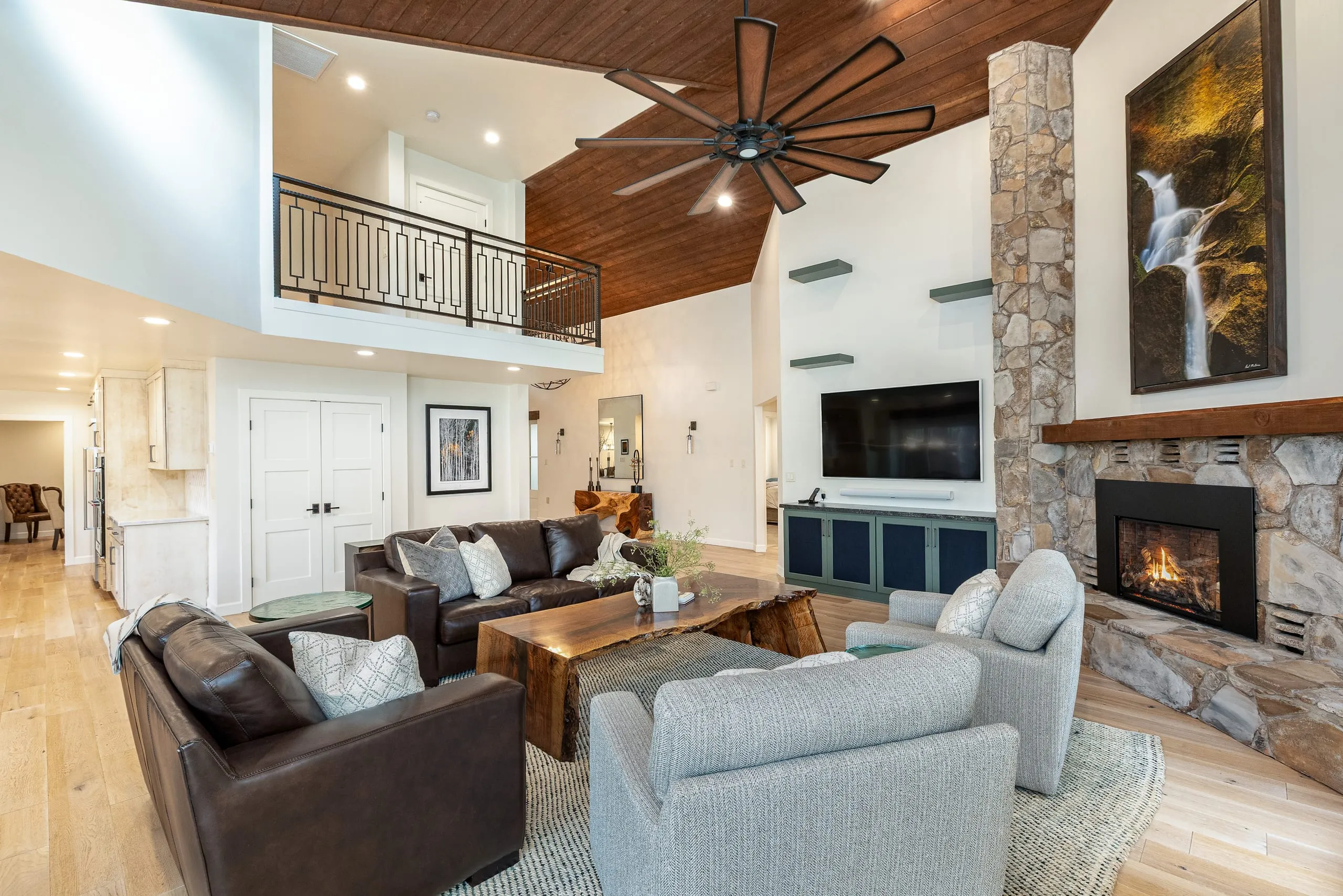 Open living area with leather sofas, a stone fireplace and a balcony overlook