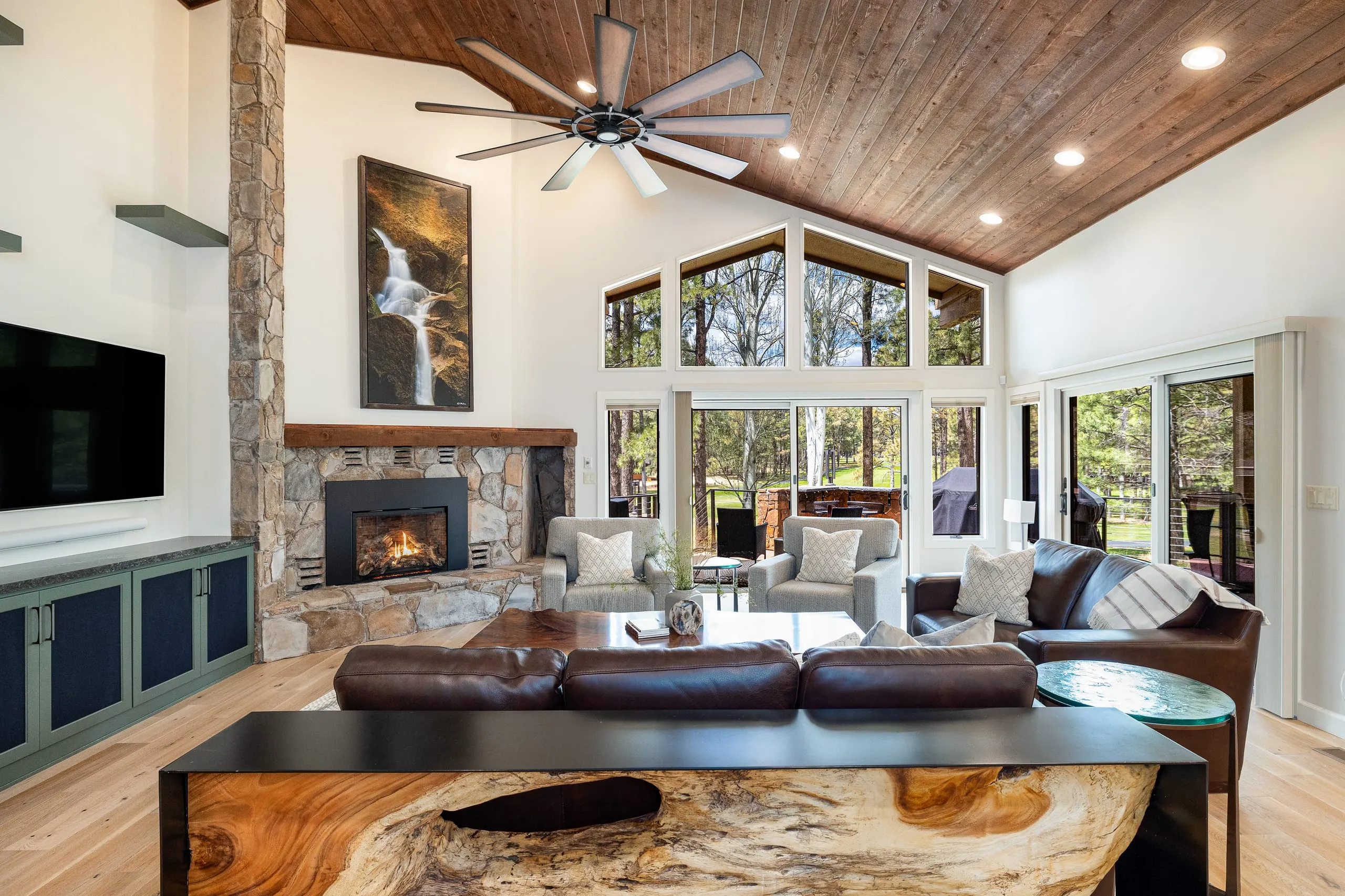 Great room with a live-edge table, stone fireplace and a wall of windows