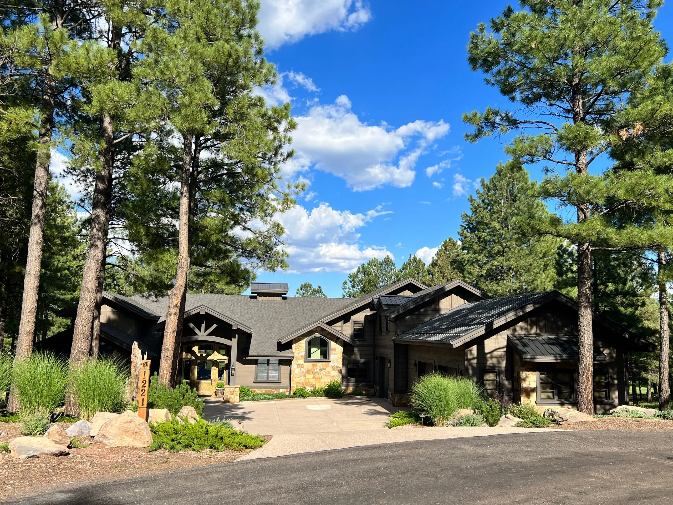 Low dark-sided home among pines with a curving drive and native plantings