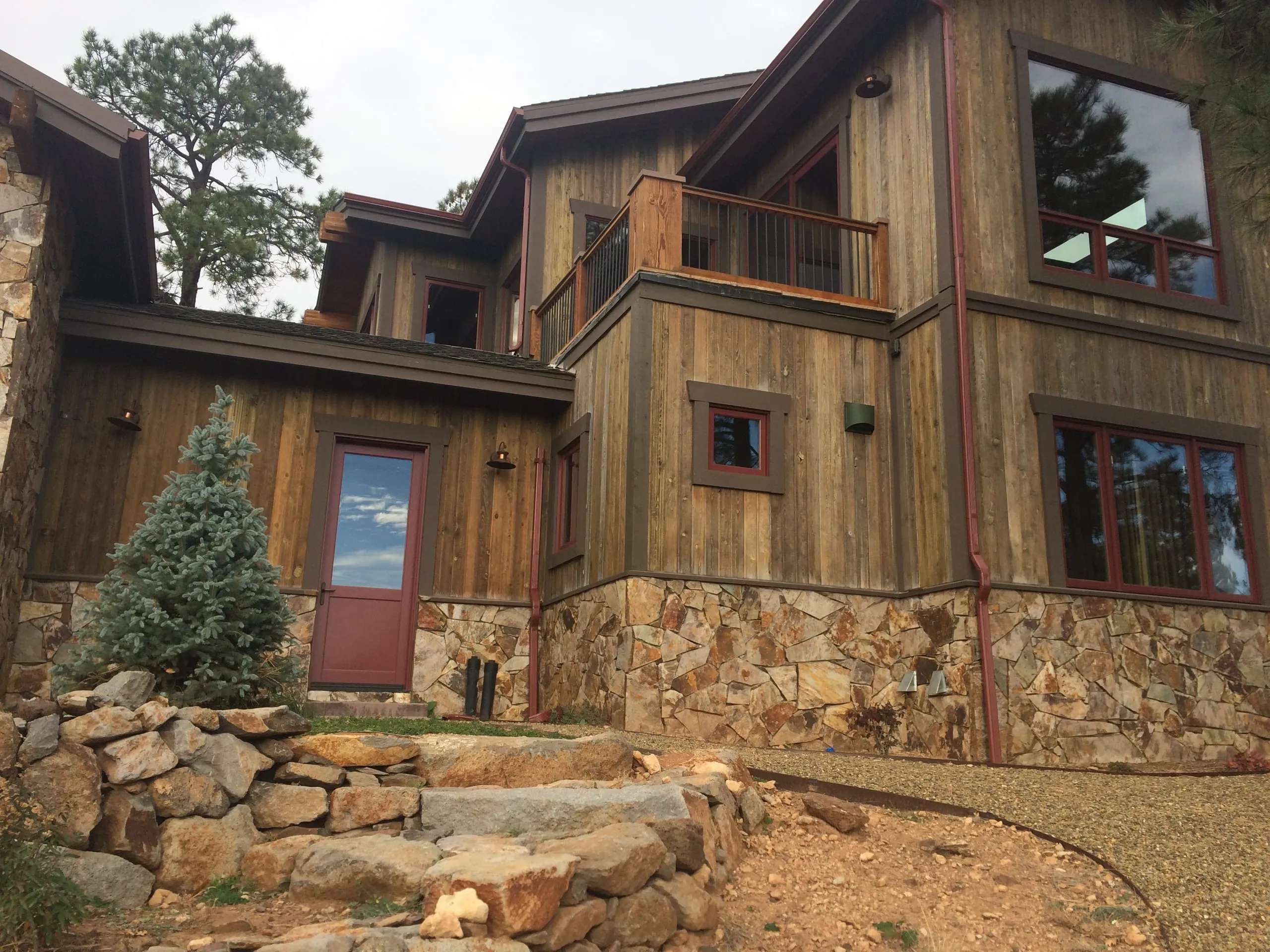 Rustic home with weathered wood siding, a stone base and a red door