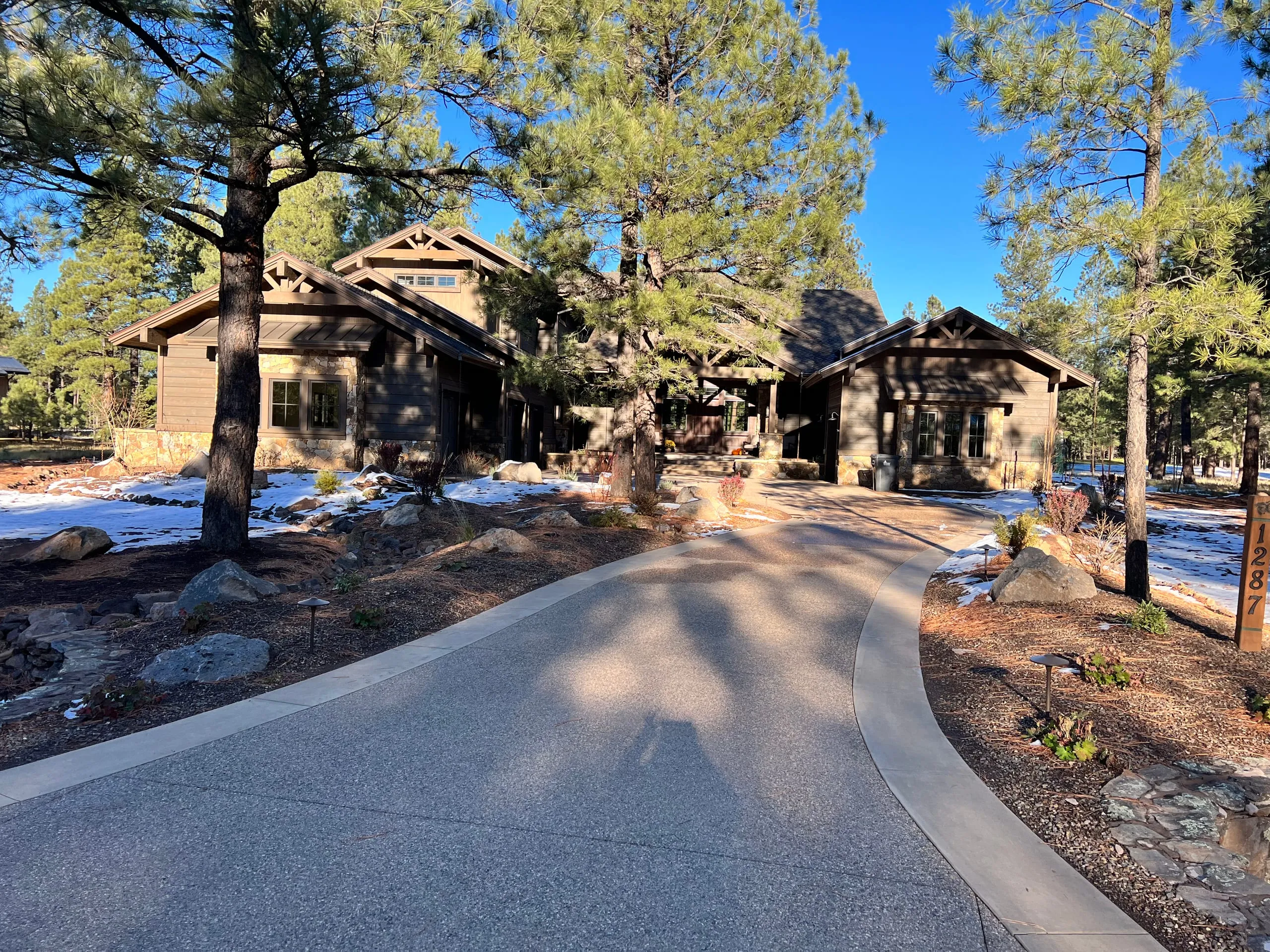 Paved drive curving toward a stone and timber home among the pines
